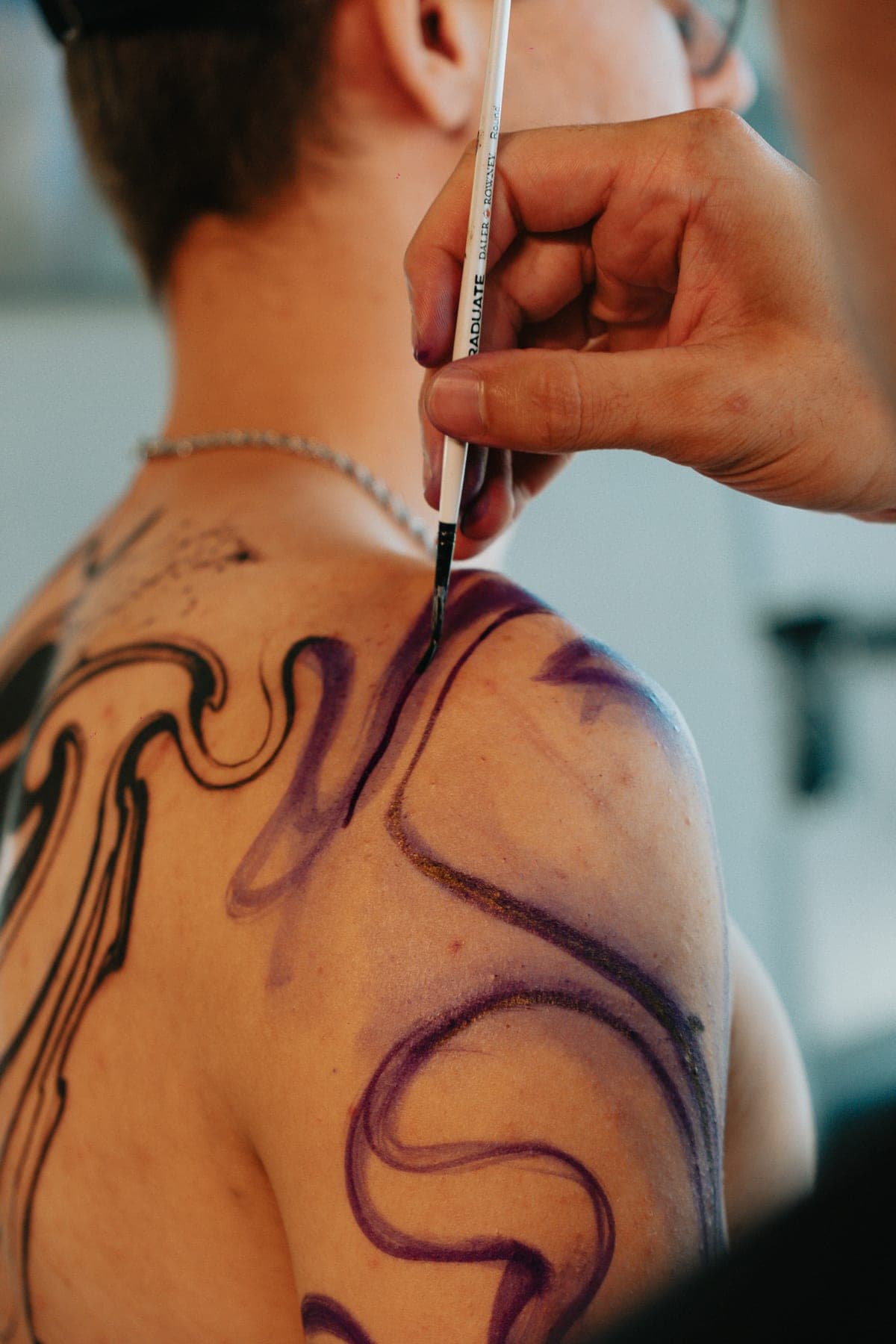 A mão de Cláudio desenhando com marcador na nuca e no ombro do cliente