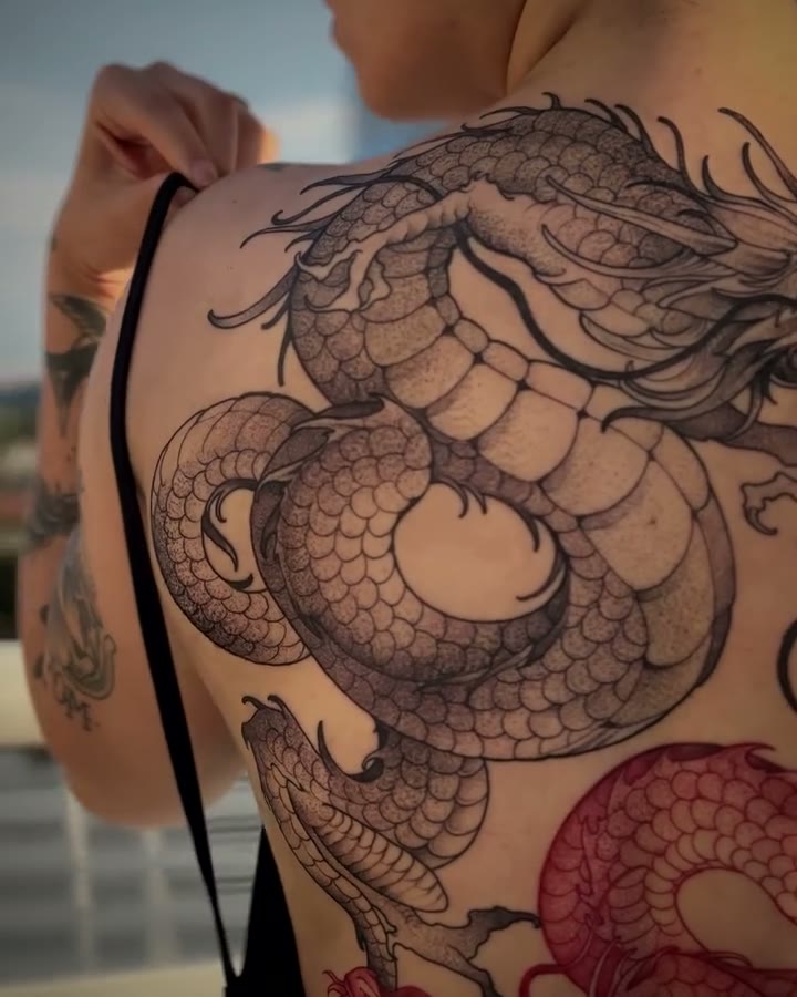 Costas fechadas com um dragão em preto e vermelho, cliente de pé com a cidade ao fundo